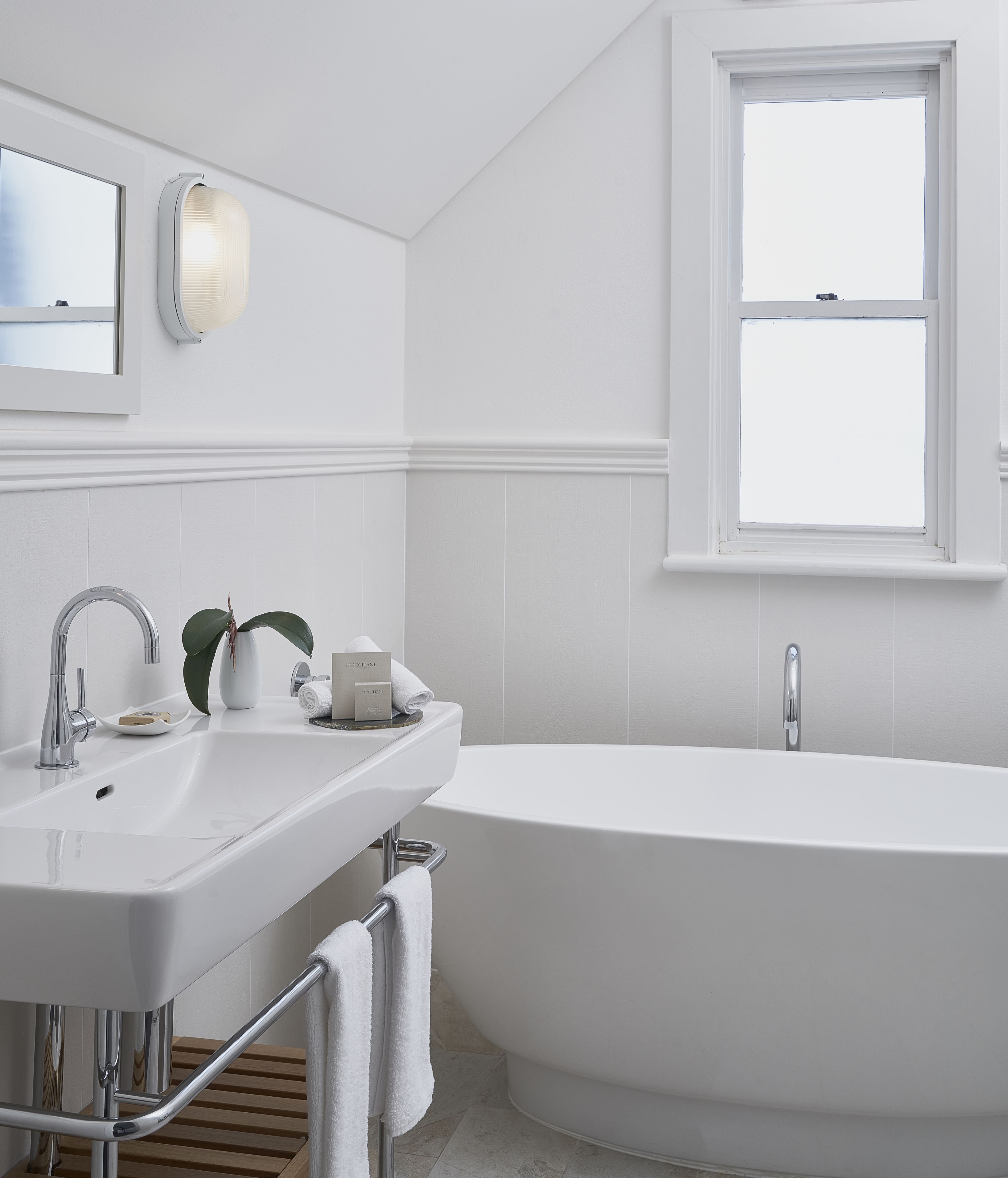 Une salle de bain moderne avec une baignoire sur pieds, un lavabo avec un miroir et une fenêtre située au-dessus de la baignoire.
