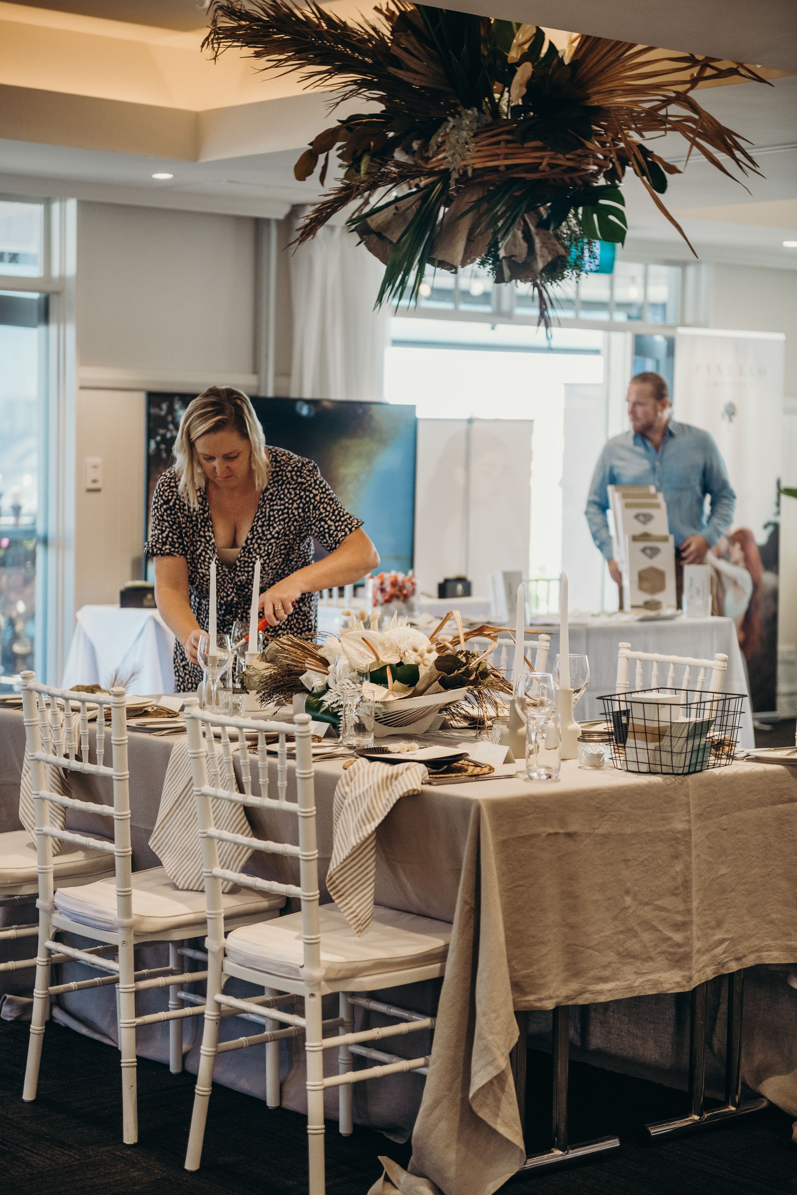 A dining area with white chairs and a table set for a meal, featuring a centerpiece and candles.