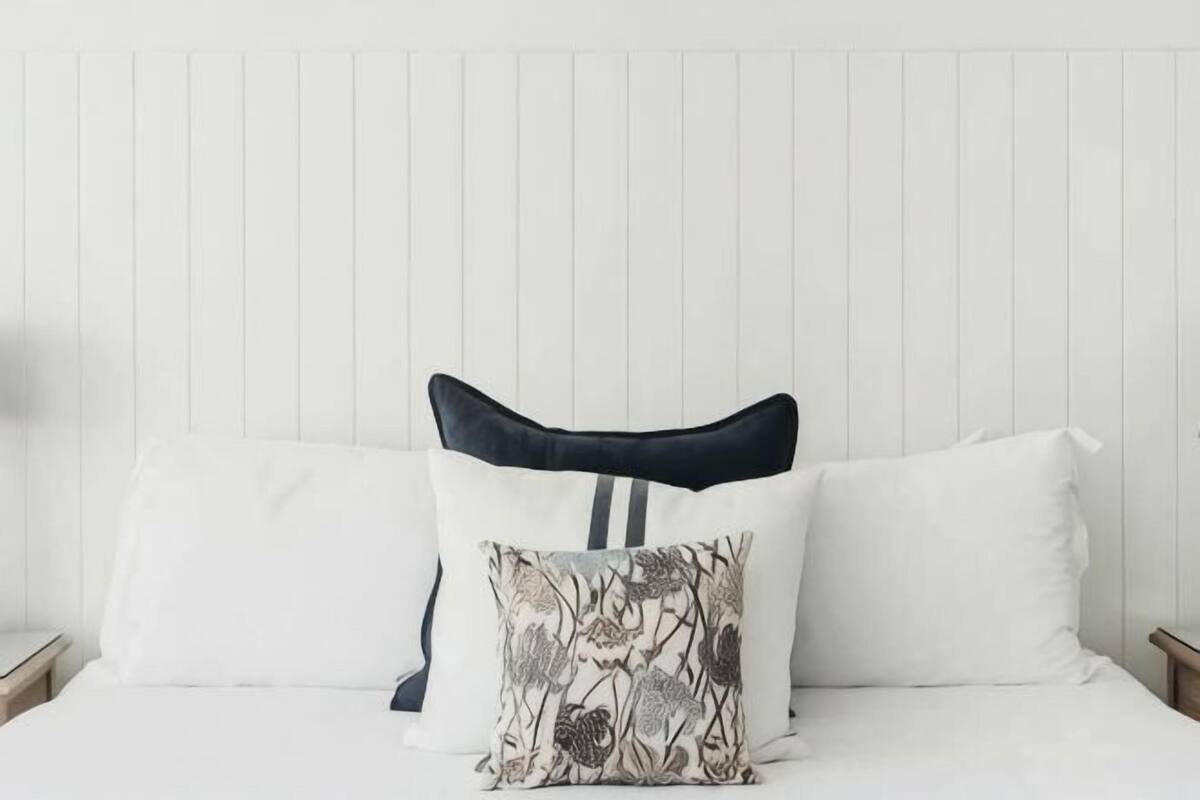 A bed with white bedding and two pillows, one with a floral pattern.