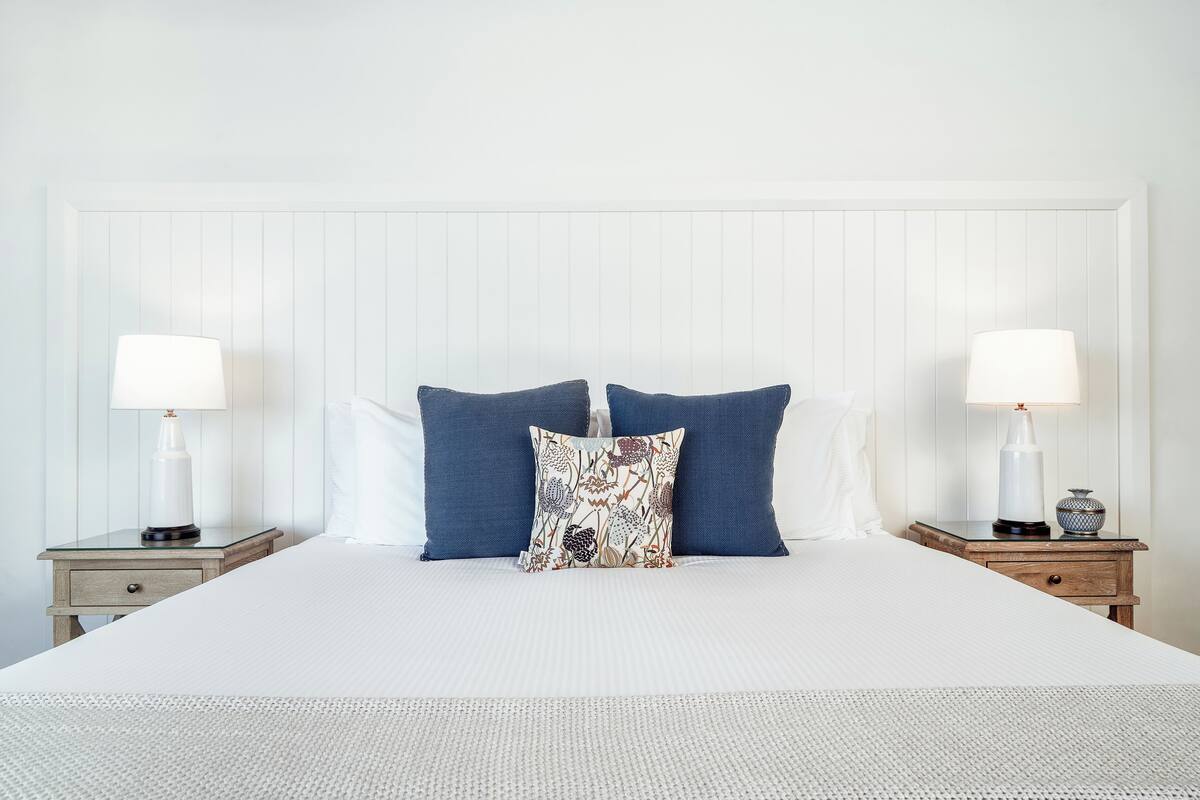 A neatly made bed with two pillows, two bedside tables with lamps, and a white headboard.