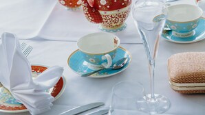 A table set with tea service, including teapots, cups, saucers, and a glass.