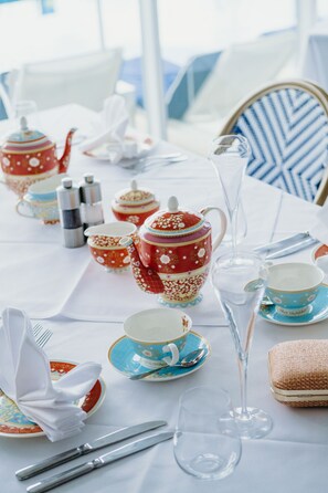A table set with tea service, including teapots, cups, saucers, and a glass.