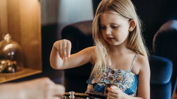 A child playing chess on a round table in a room with wooden walls and a dark armchair.