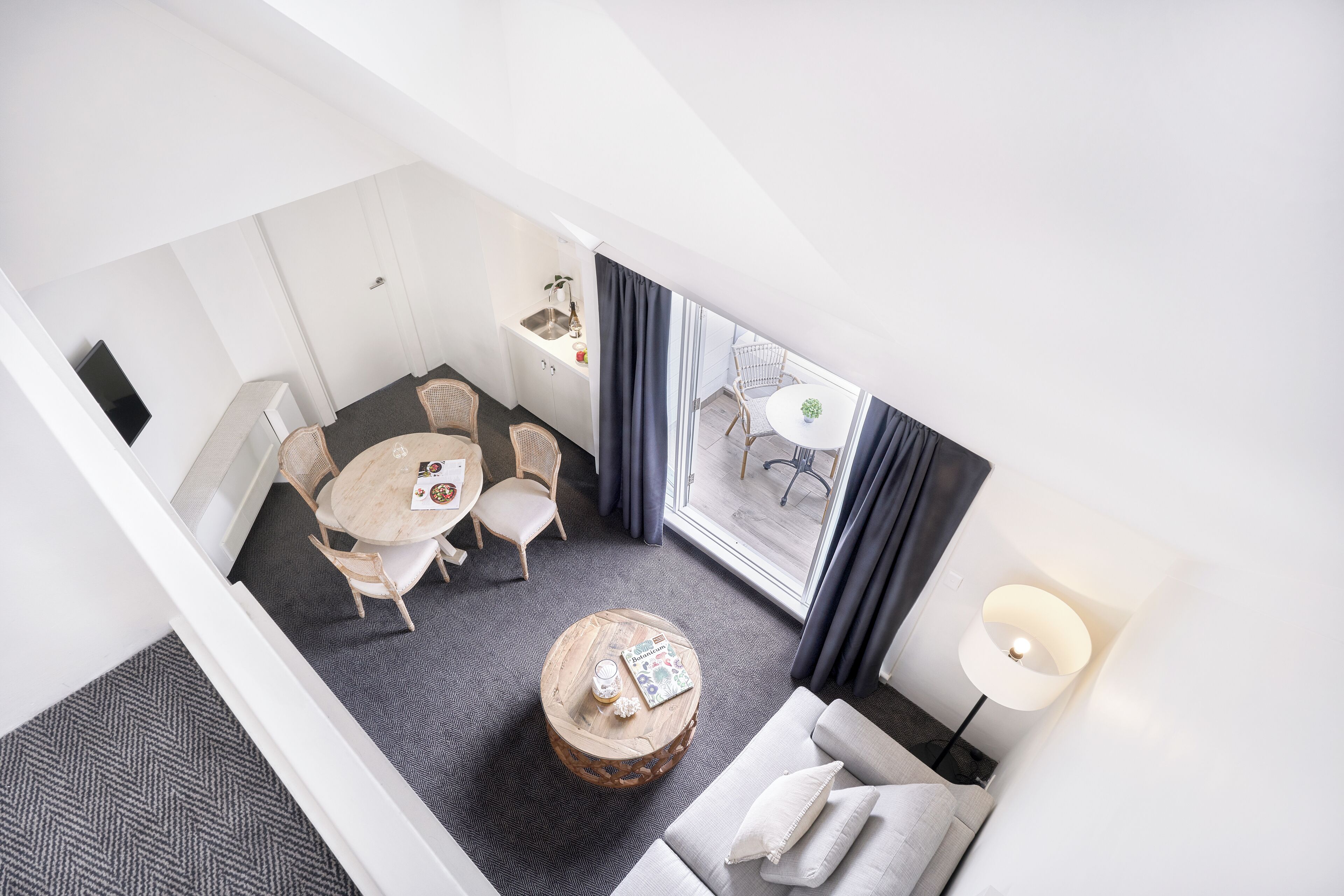 A hotel room with a dining area, a round wooden coffee table, a sofa, a lamp, and a view of the outside.