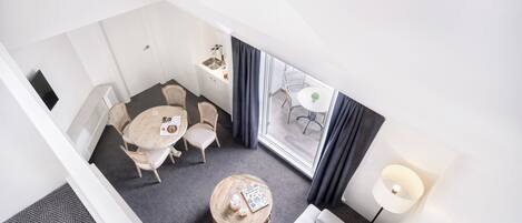 A hotel room with a dining area, a round wooden coffee table, a sofa, a lamp, and a view of the outside.