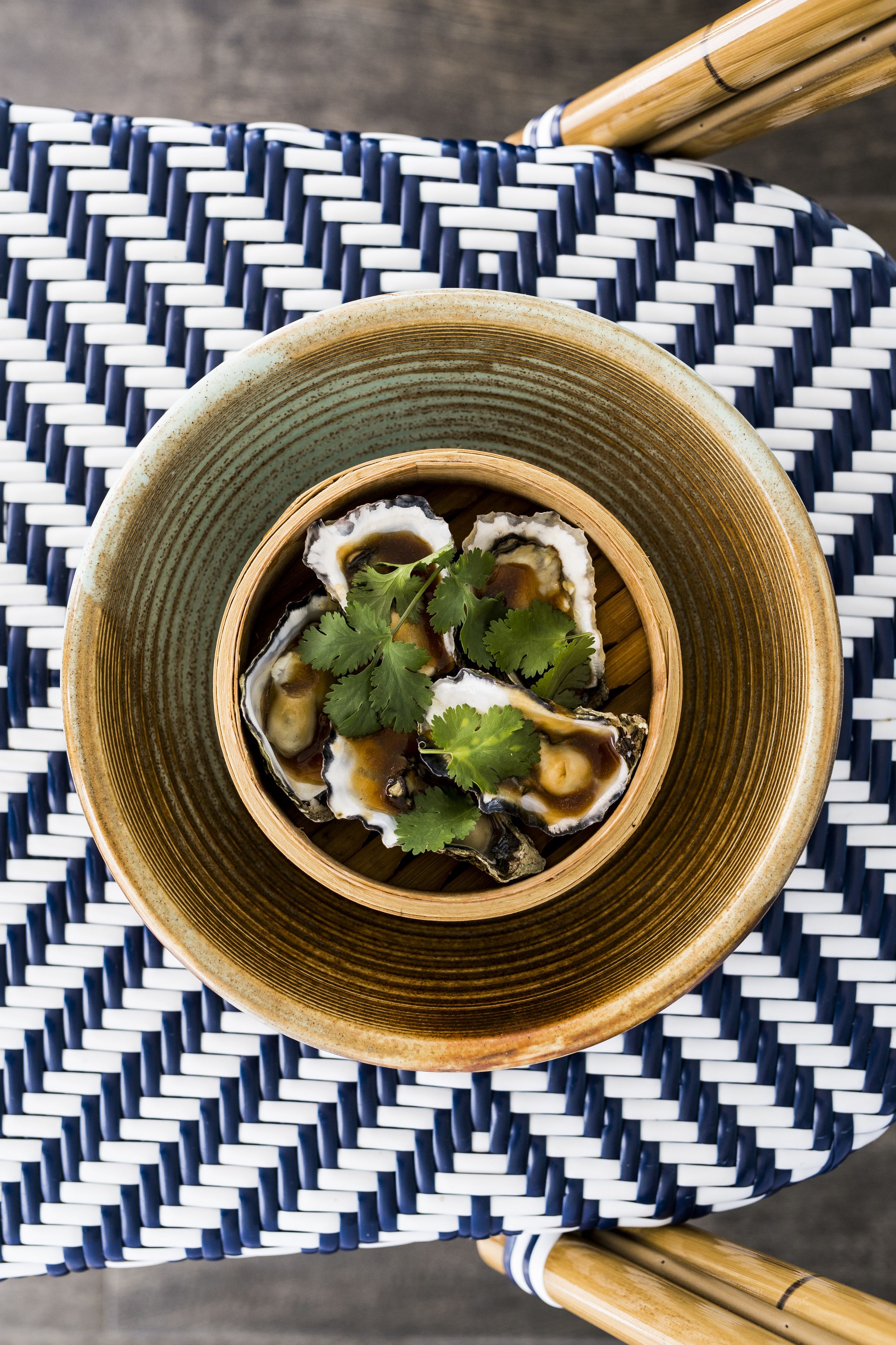 A bowl of oysters with sauce and cilantro on a woven mat.