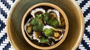 A bowl of oysters with sauce and cilantro on a woven mat.
