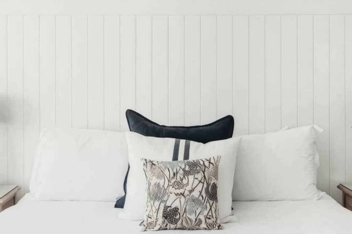 A bed with white bedding and two pillows, one with a floral pattern.