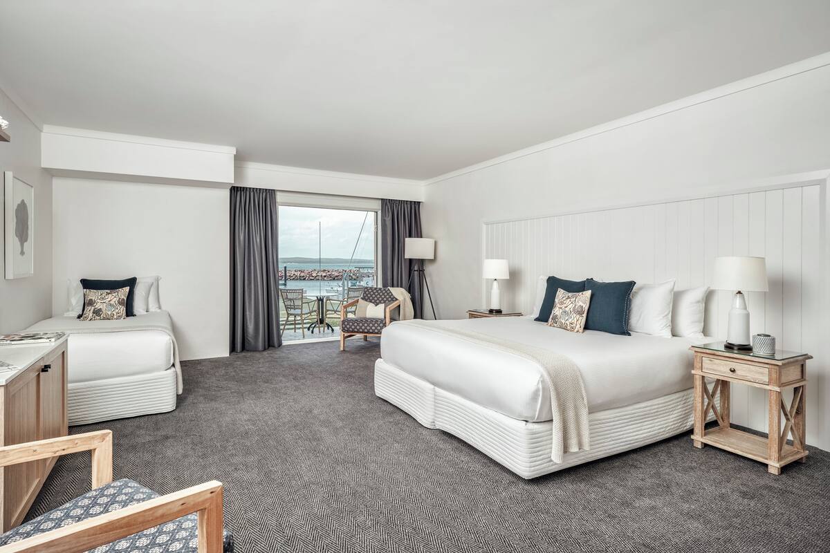 A hotel room with a large bed, a desk, a chair, and a view of the sea.