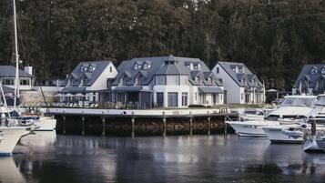 A marina with several boats docked, a dock with a covered walkway, and a row of houses with gabled roofs.