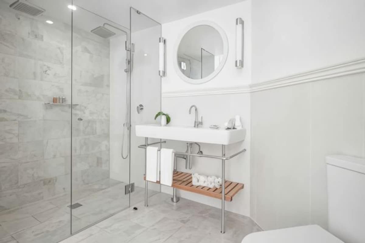 A modern bathroom with a glass shower enclosure, a white sink with a mirror, and a wooden shelf.