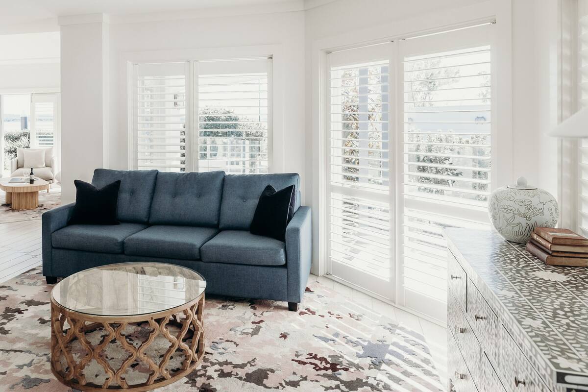A modern living room with a blue sofa, a glass coffee table, and a patterned rug.
