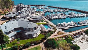 A marina with multiple boats docked, a large house with a swimming pool, and a rocky coastline. - Anchorage Port Stephens (Corlette)
