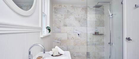 A modern bathroom with a white sink, a mirror, a glass-enclosed shower, and a marble-tiled wall.