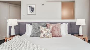 A hotel room with a large bed, two bedside tables with lamps, a gray headboard, and a framed picture on the wall.