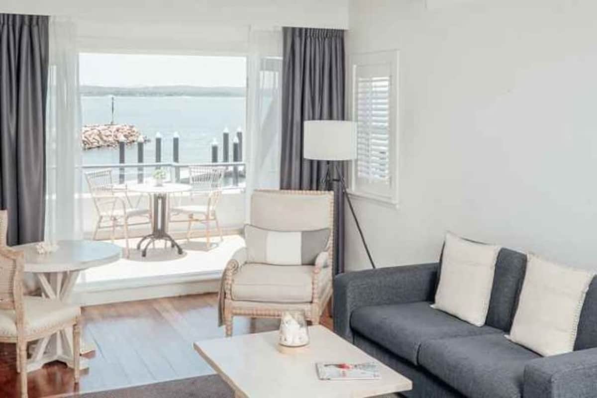 A living room with a sofa, a coffee table, and a view of the sea through large windows.