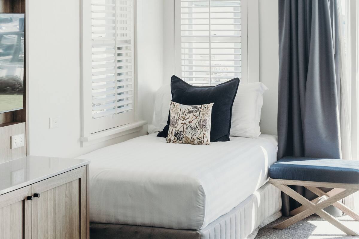A bedroom with a bed, a bedside table, a wardrobe, and a window with blinds.