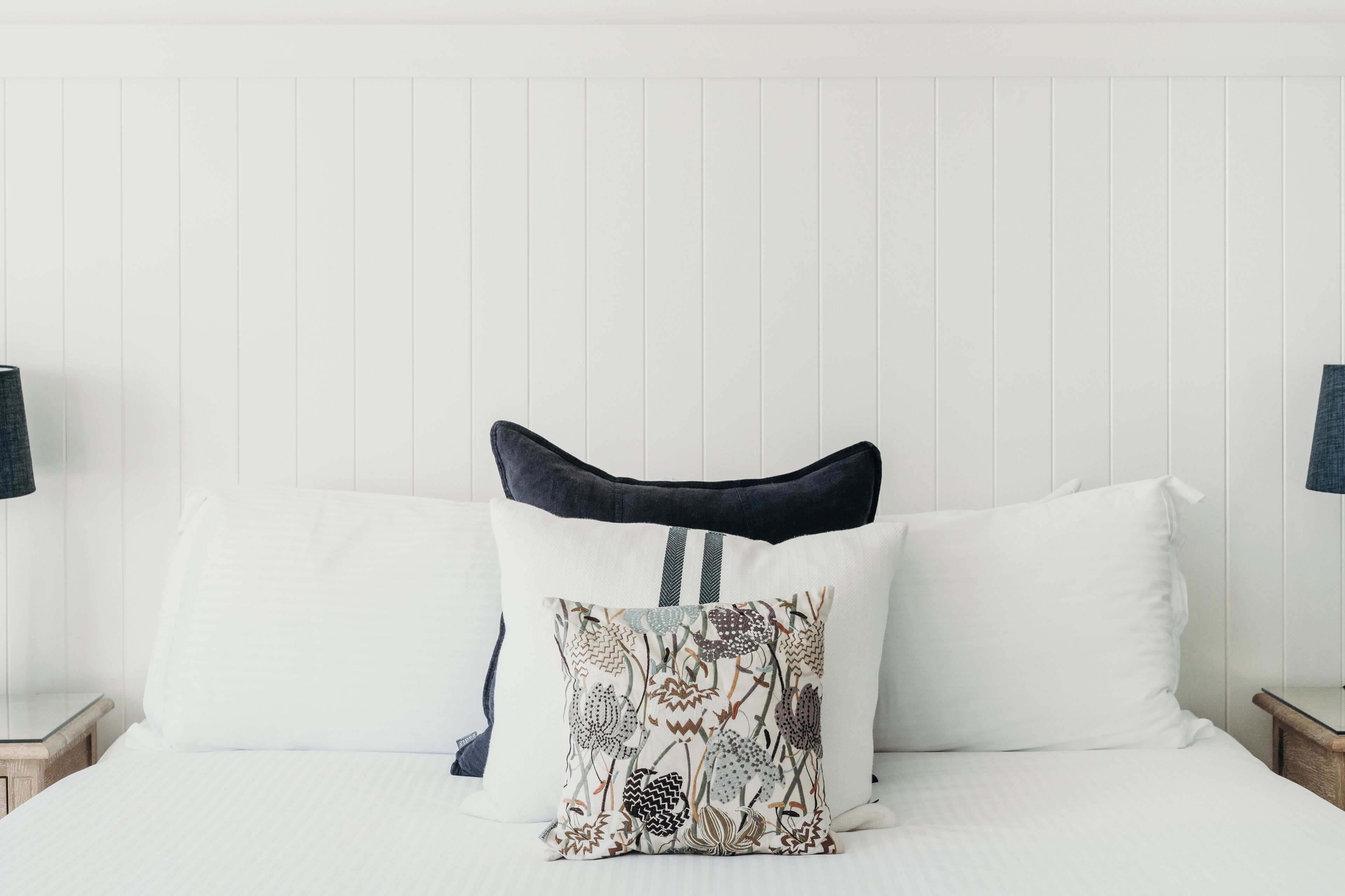 A neatly made bed with white linens, a decorative pillow with a nature pattern, and a dark headboard.