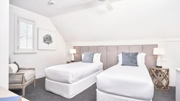 Habitación de hotel con dos camas, un ventilador de techo, una ventana con persianas, una obra de arte en la pared y una mesita de noche con lámpara.