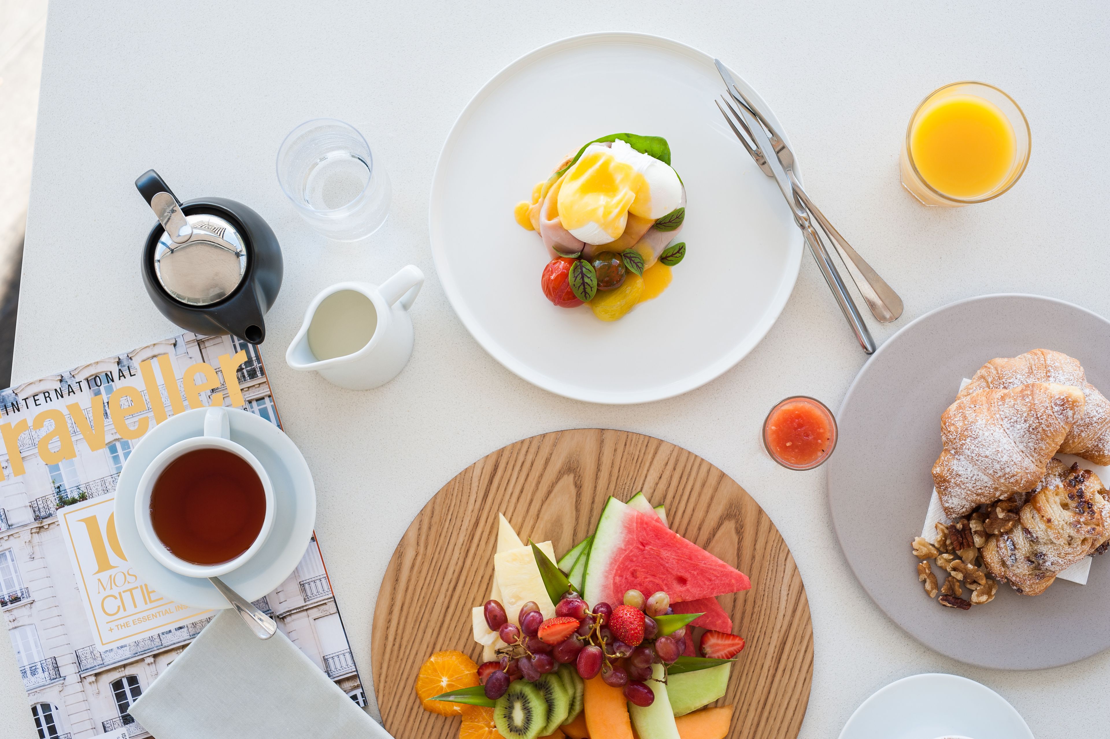 Un desayuno con un croissant, una bandeja de fruta, café y un periódico.