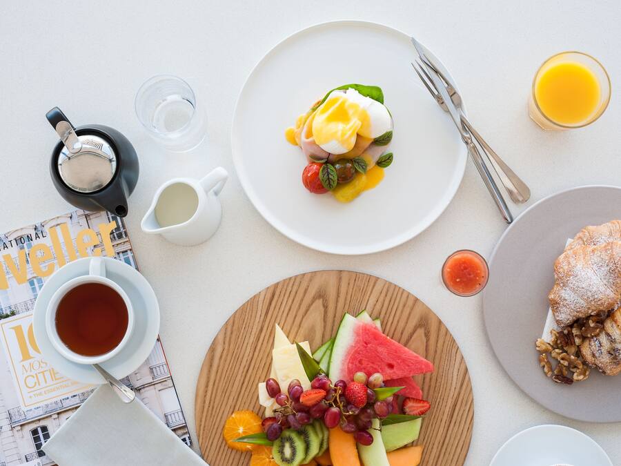Un desayuno con un croissant, una bandeja de fruta, café y un periódico.