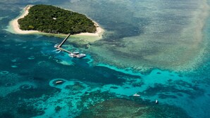 Vista aérea de una isla tropical con aguas turquesas cristalinas, una playa de arena y un muelle con barcos.