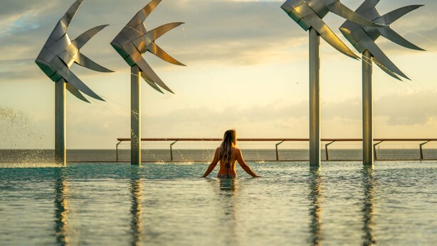 Una persona está de pie en una piscina, con grandes aerogeneradores al fondo.