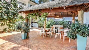 An outdoor patio with a wooden pergola, brick flooring, and white furniture.