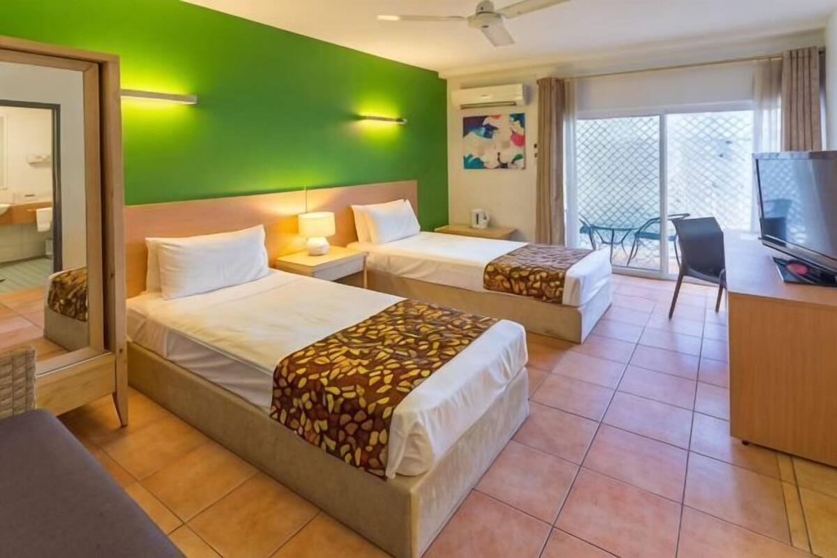 A hotel room with two beds, a TV, a desk, and a balcony with a view.