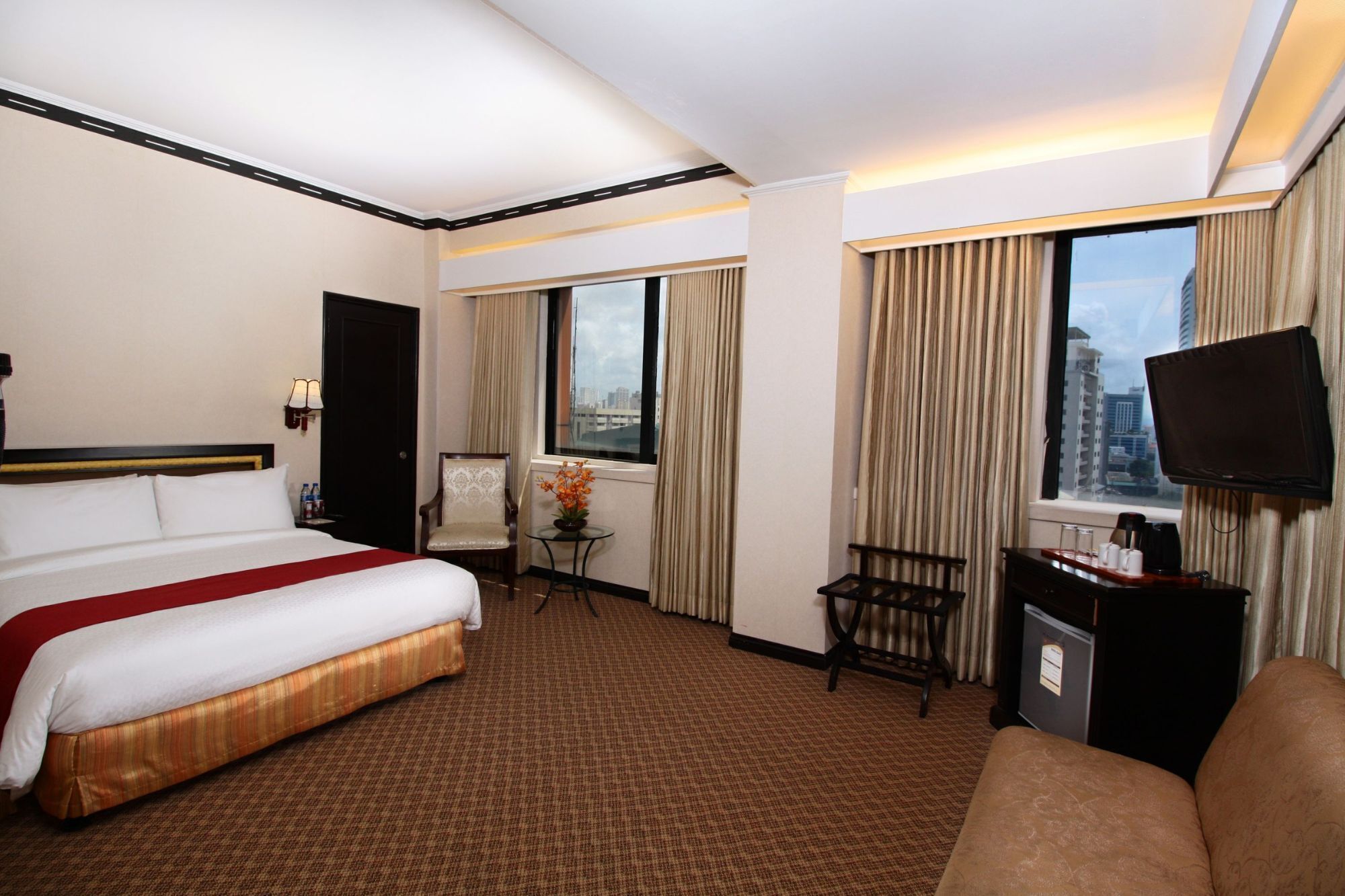 A hotel room with a bed, a desk, a chair, a TV, and a window with curtains.