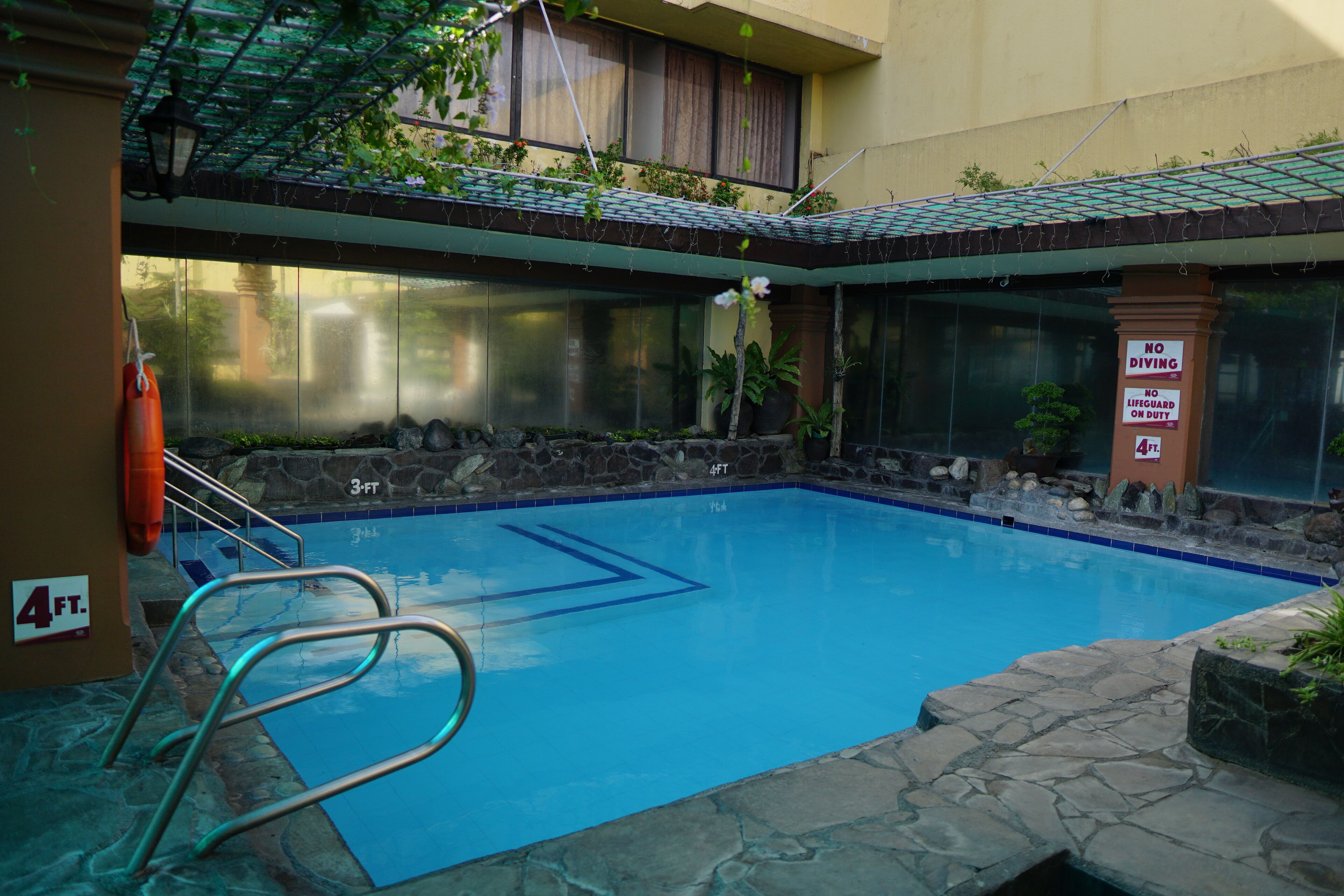 A swimming pool with a 4-foot depth marker, surrounded by stone walls and potted plants.