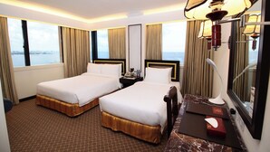 A hotel room with two beds, a marble desk, a lamp, and a view of the sea. - Bayview Park Hotel Manila (Manila)