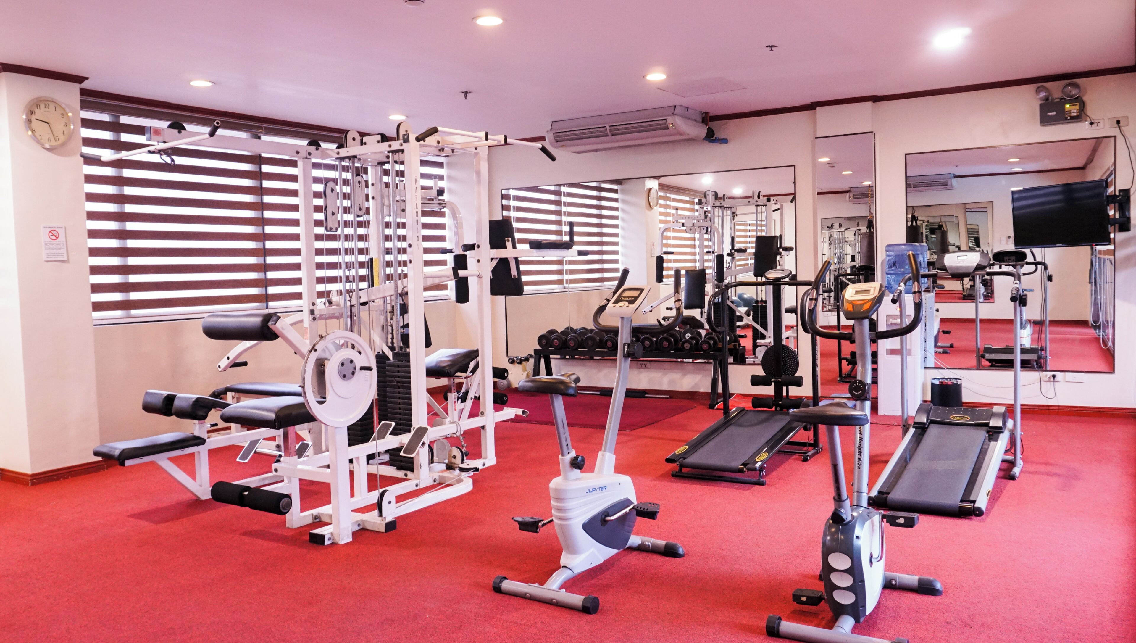 Ein Fitnessstudio mit verschiedenen Trainingsgeräten, darunter Laufbänder, Kraftgeräte und Kurzhanteln.