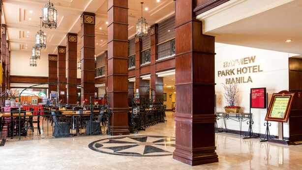 A lobby with high wooden columns, chandeliers, and a central geometric floor design. - Bayview Park Hotel Manila (Manila)
