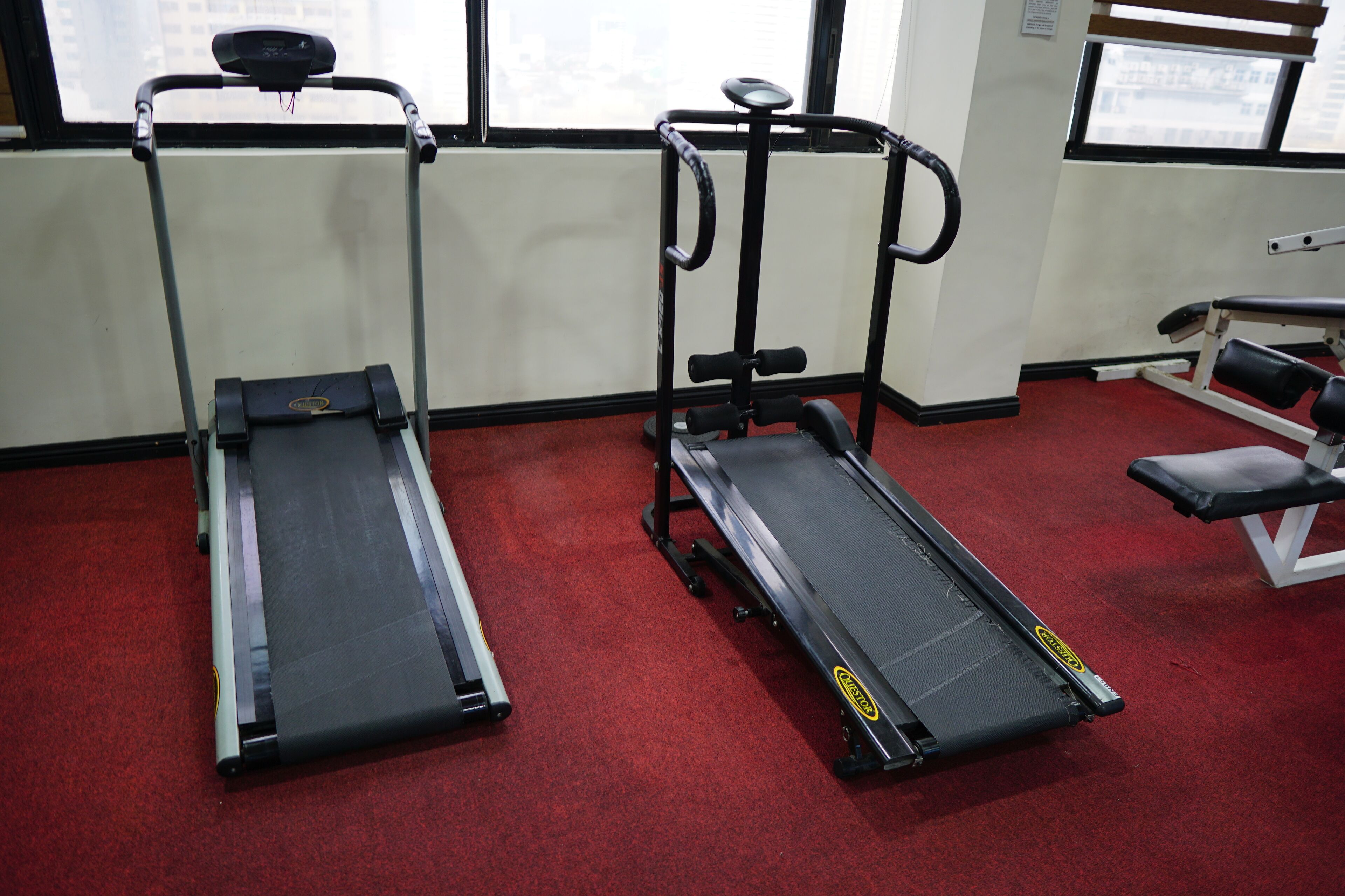 Une salle de sport équipée de tapis de course, d’une machine de musculation et d’un banc.