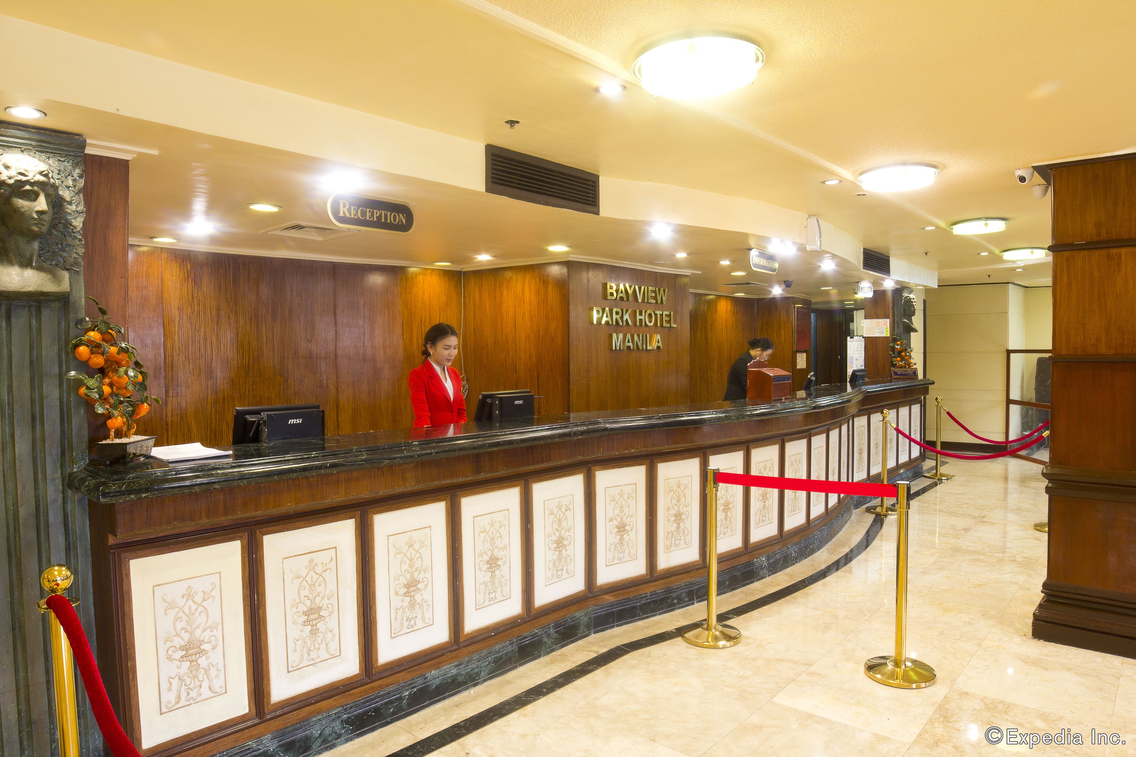 A reception desk at Bayview Park Hotel Manila with a receptionist, a sign indicating the reception area, and a red rope barrier.
