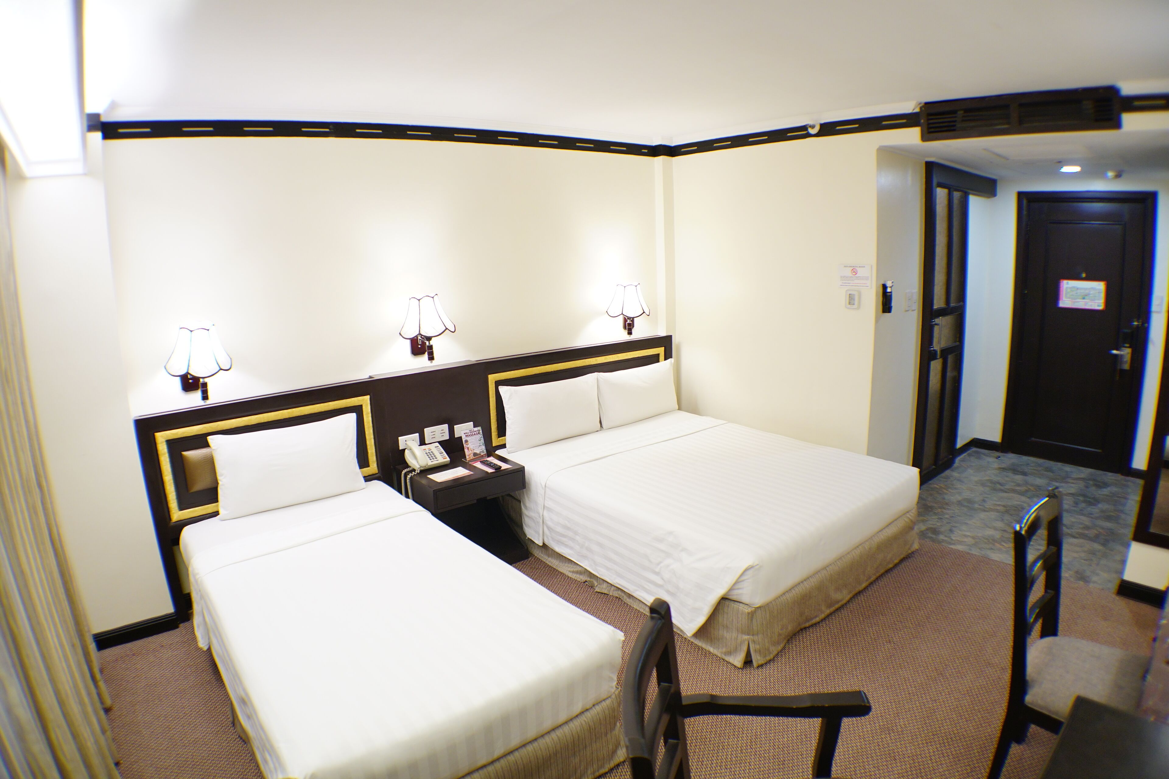 A hotel room with two single beds, a desk with a telephone, and a chair.