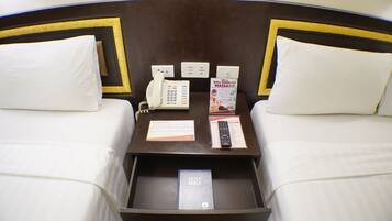 Habitación de hotel con dos camas, una mesita de noche con un teléfono, un control remoto y un folleto.