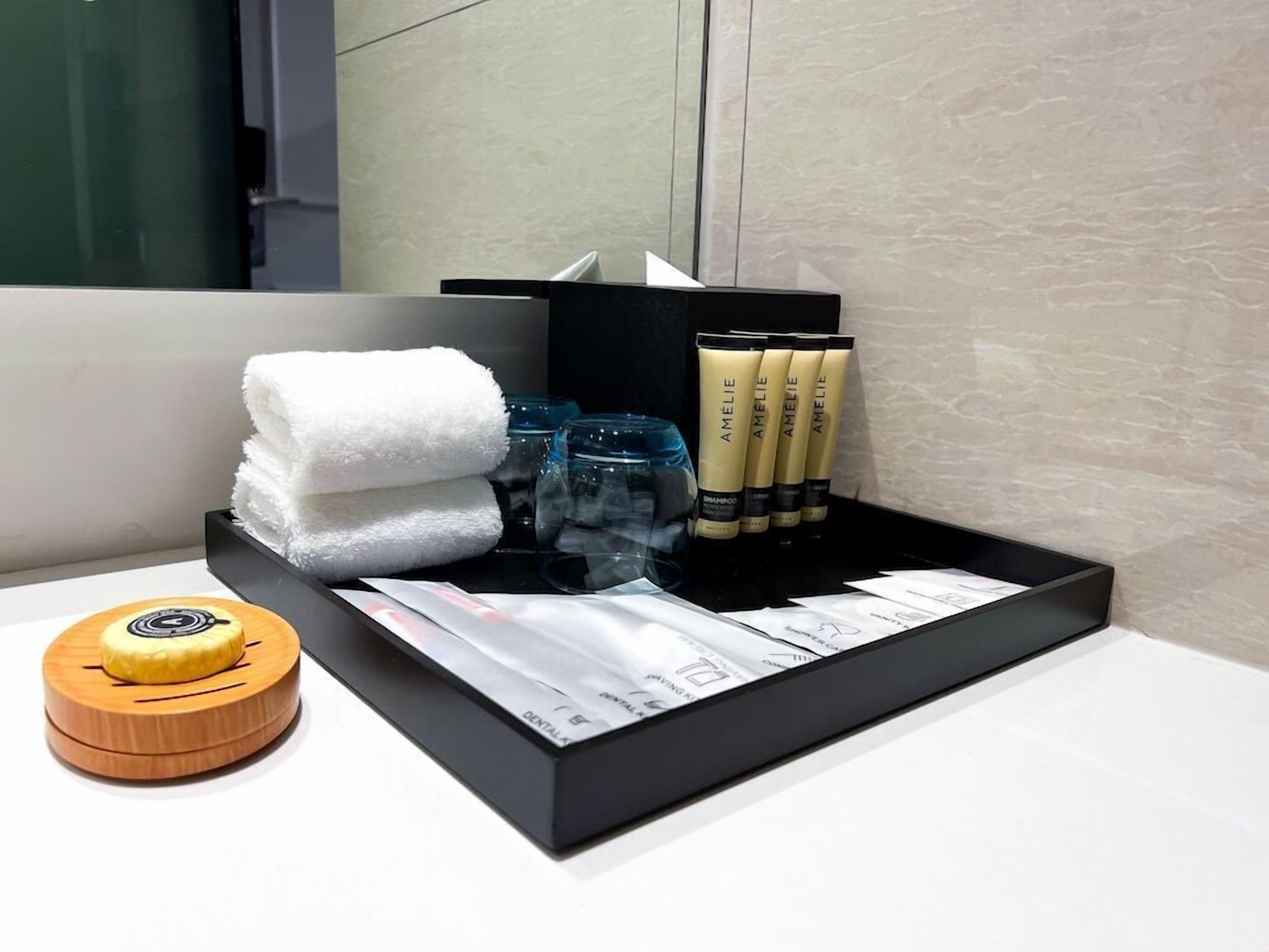 Bany d'hotel amb una safata negra que conté productes de tocador, una tovallola blanca i un suport per al raspall de dents.