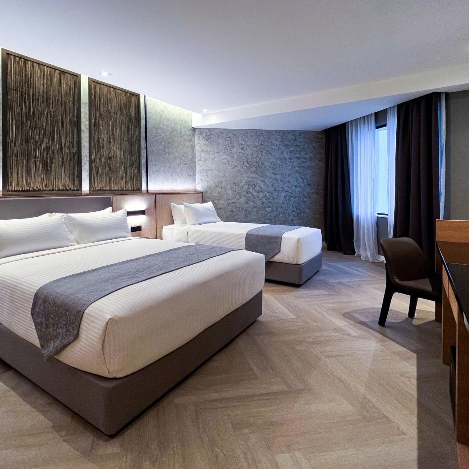 A hotel room with a large bed, a smaller bed, a desk, and a chair.
