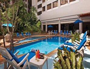 A pool area with lounge chairs and umbrellas, surrounded by greenery and a building with multiple floors. - Royale Chulan Bukit Bintang (Kuala Lumpur)