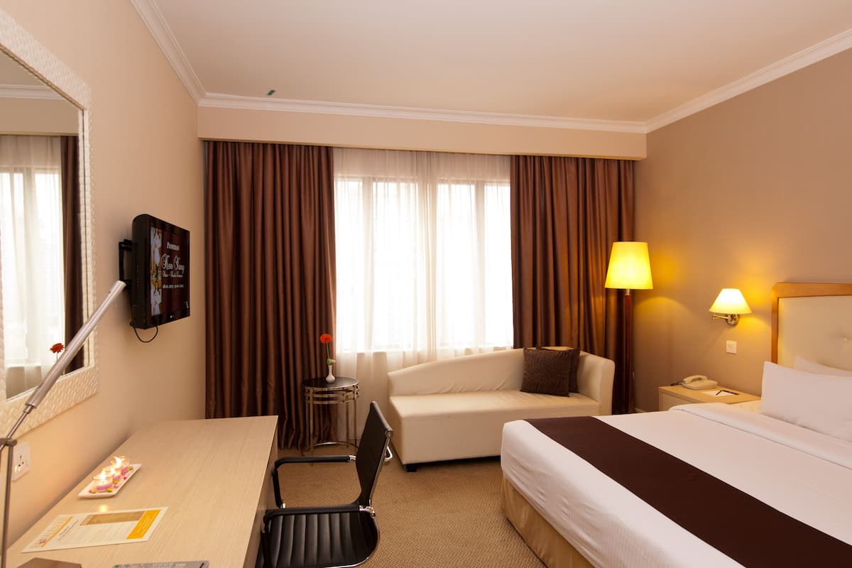 A hotel room with a bed, a desk, a chair, a lamp, and a TV.