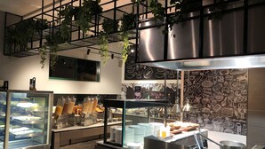 A buffet area with a glass display case, a coffee station, and a wall with food illustrations.