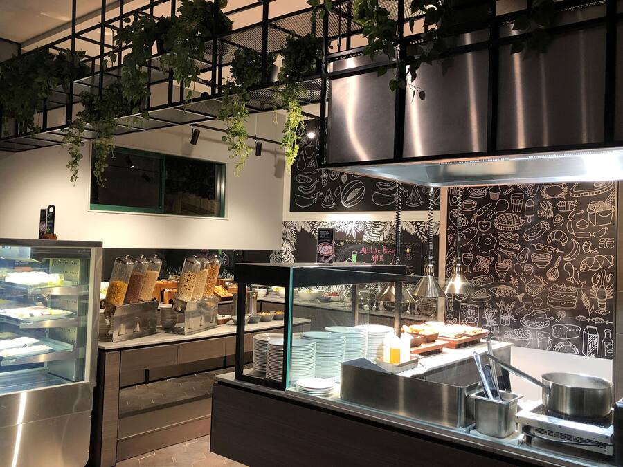 A buffet area with a glass display case, a coffee station, and a wall with food illustrations.