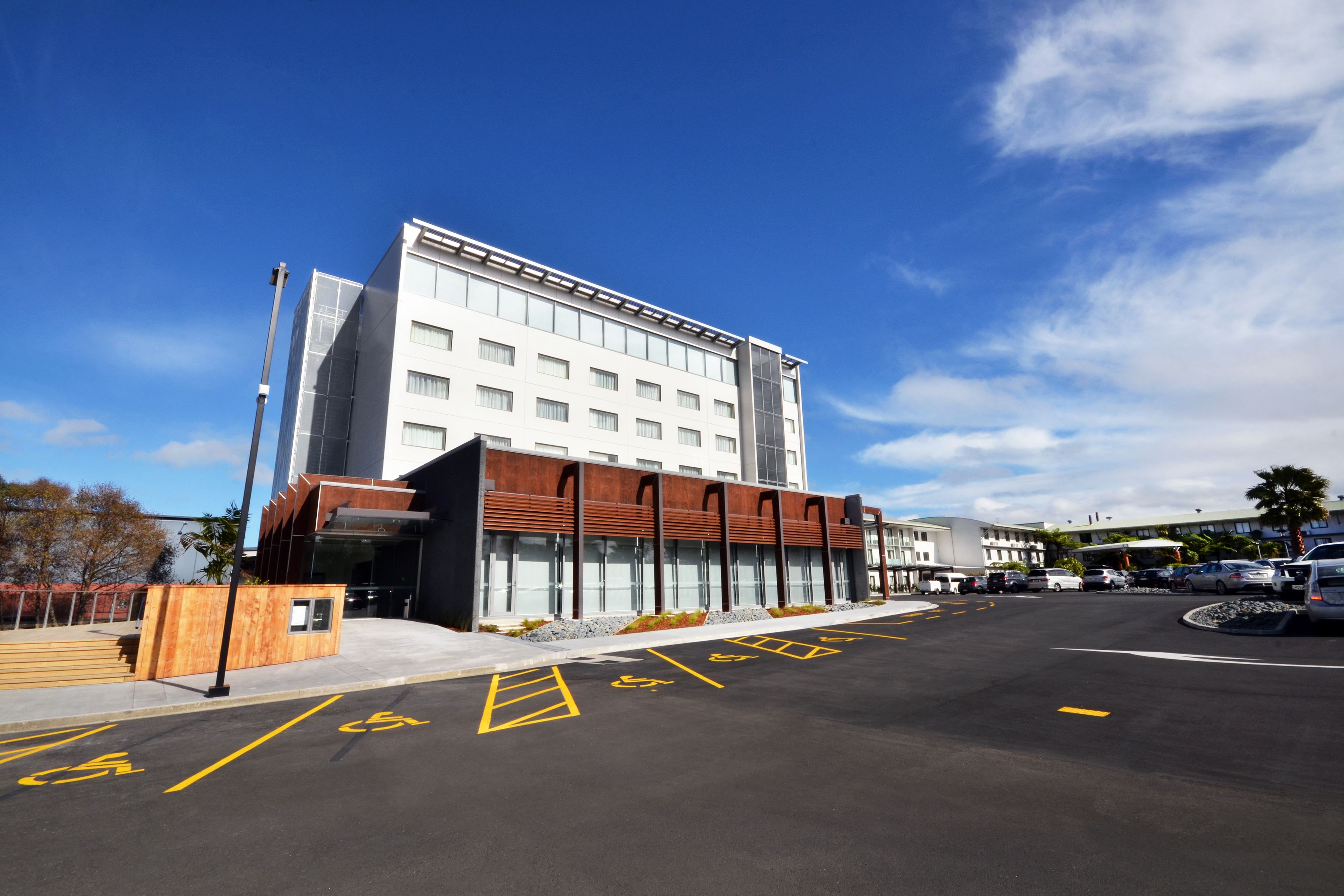 Un hotel moderno con techo plano, grandes ventanales y un estacionamiento con espacios reservados para discapacitados.