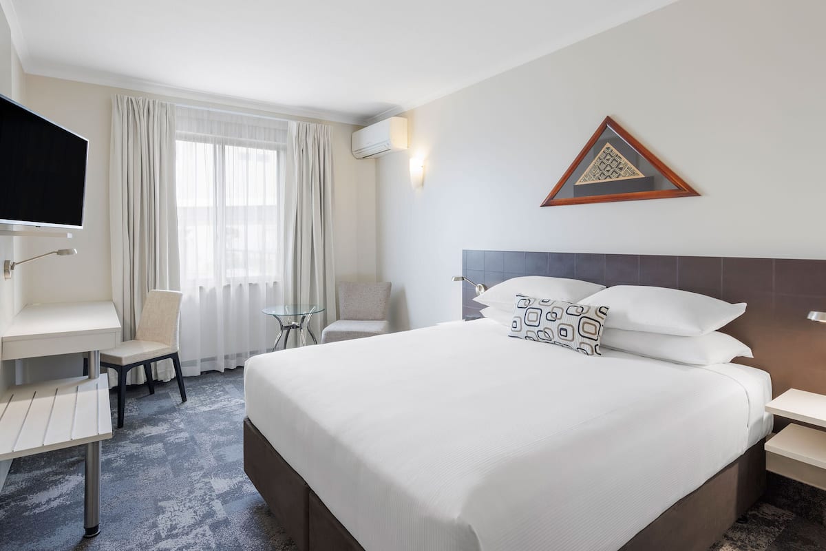A hotel room with a large bed, a desk with a chair, a TV, and a window with curtains.