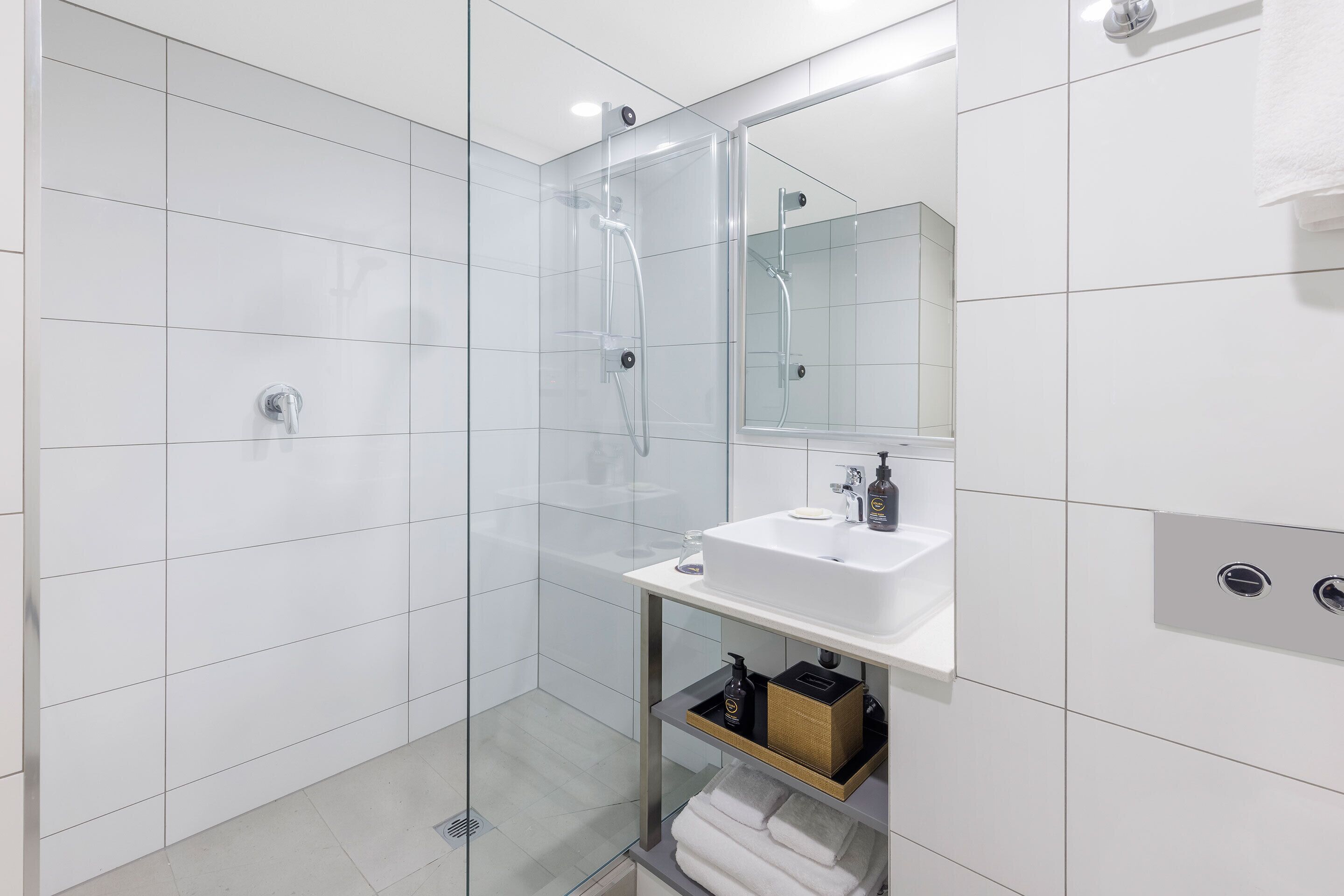 Un baño moderno con ducha de vidrio, un lavabo blanco y un espejo encima.