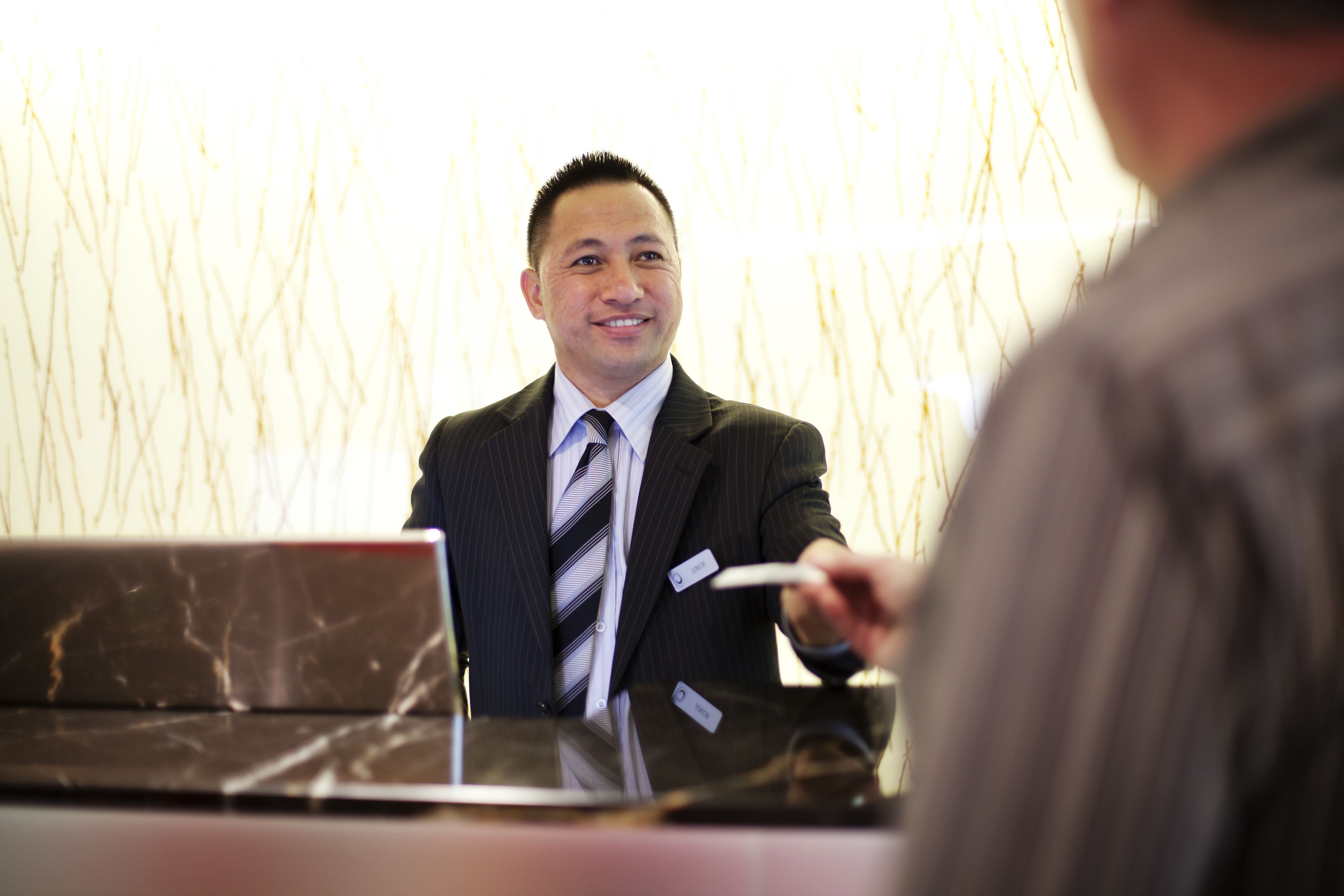 A man in a suit sitting at a desk with a laptop, holding a card.
