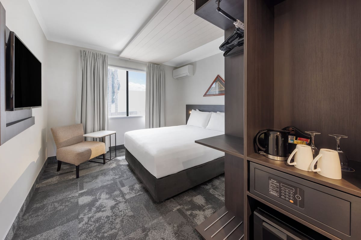 A hotel room with a bed, a chair, a small table, a TV, a coffee maker, and a microwave.
