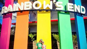 Ein farbiges Schild mit dem Schriftzug "RAINBOW'S END" und zwei Personen davor.